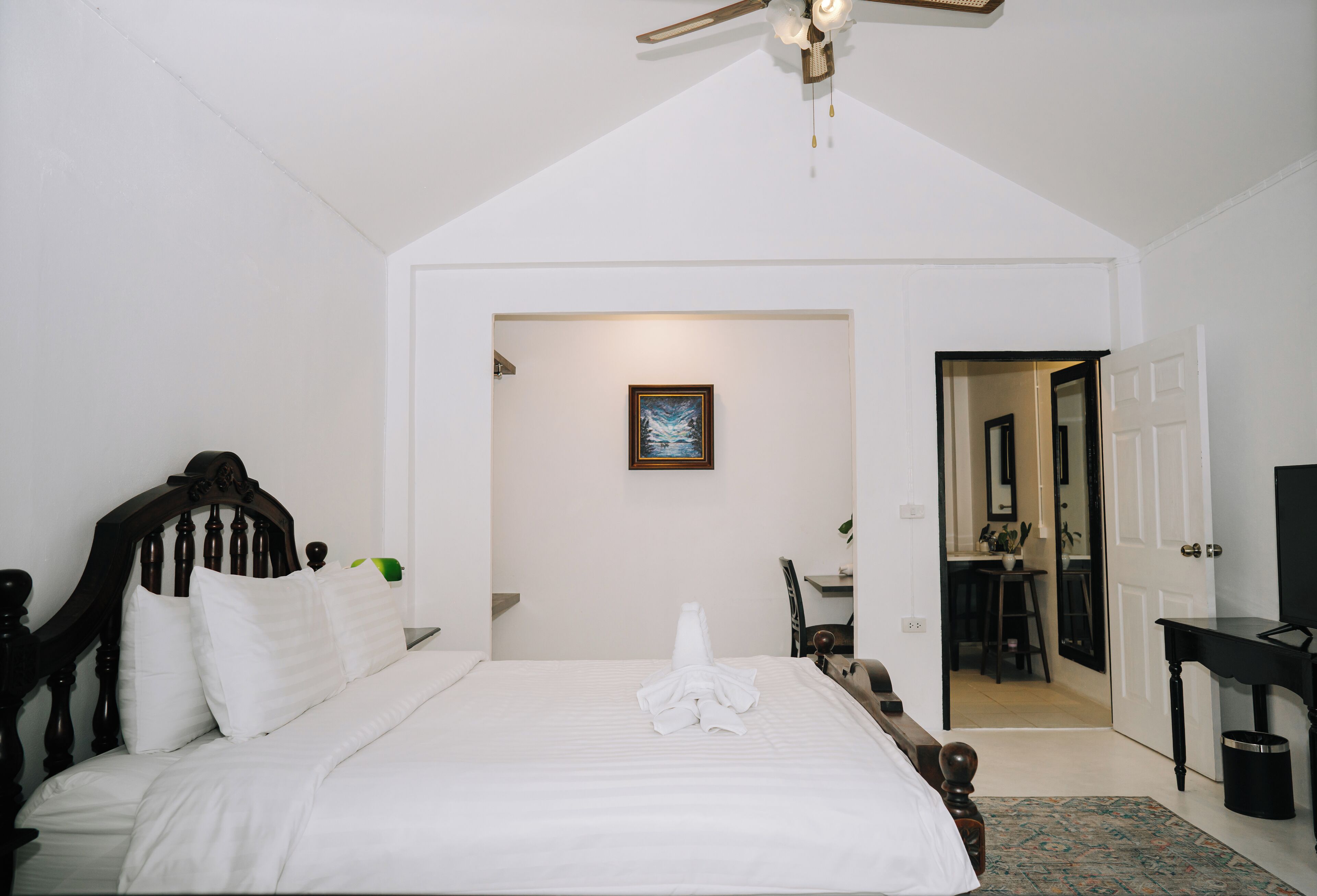 A hotel room with a large bed, a ceiling fan, a framed picture on the wall, and a door leading to a bathroom.