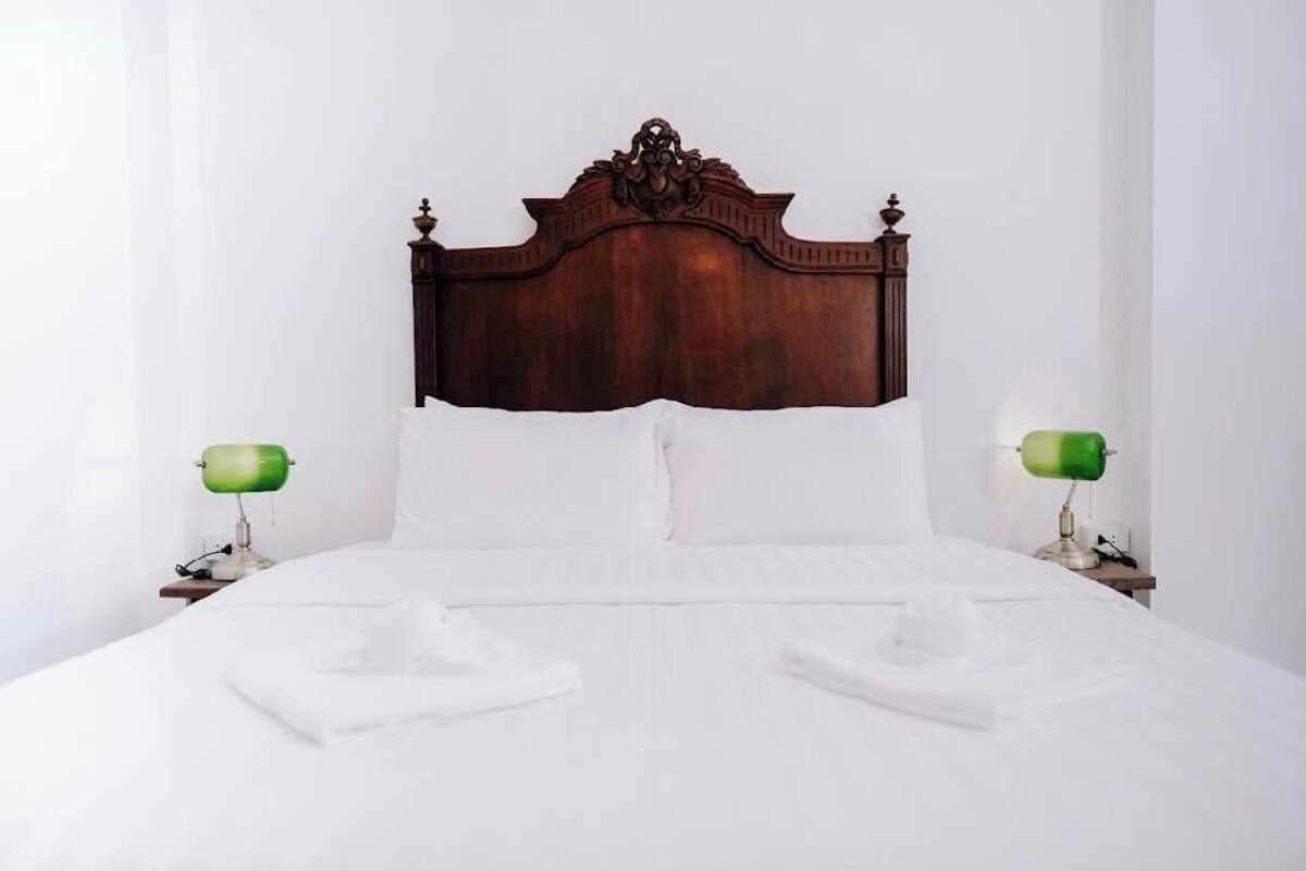 A neatly made bed with a wooden headboard, two bedside tables with lamps, and a white wall.