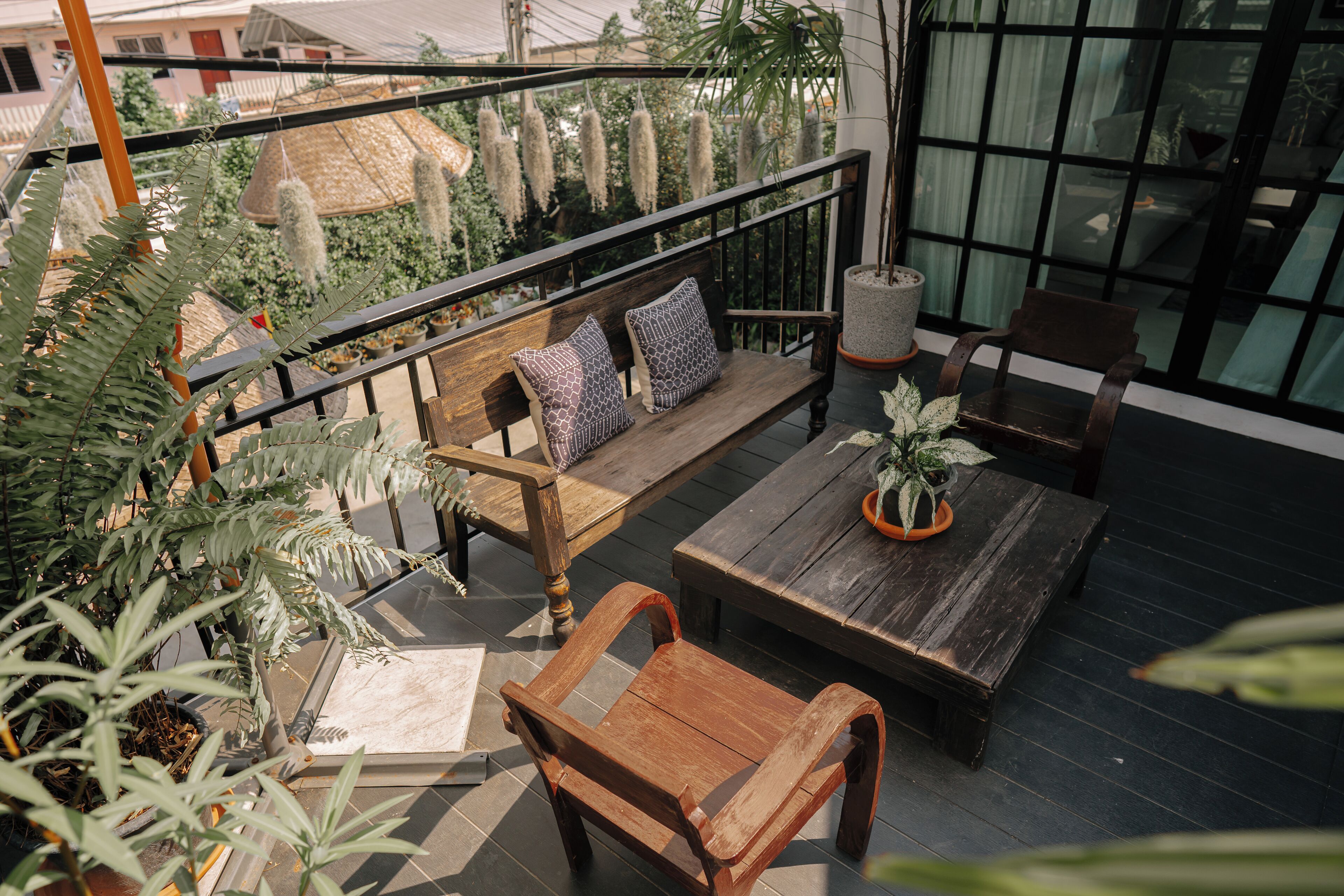 A wooden bench with cushions, a table, and potted plants on a balcony with a railing.