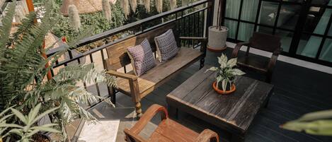 A wooden bench with cushions, a table, and potted plants on a balcony with a railing.