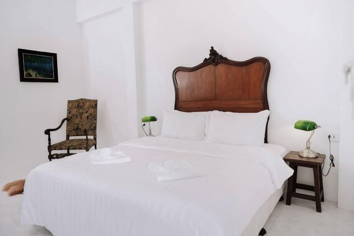 A neatly made bed with a wooden headboard, a chair with a floral pattern, and two bedside lamps.