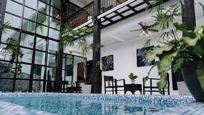 Una piscina interior con suelo de baldosas, rodeada de plantas en macetas y mobiliario negro.