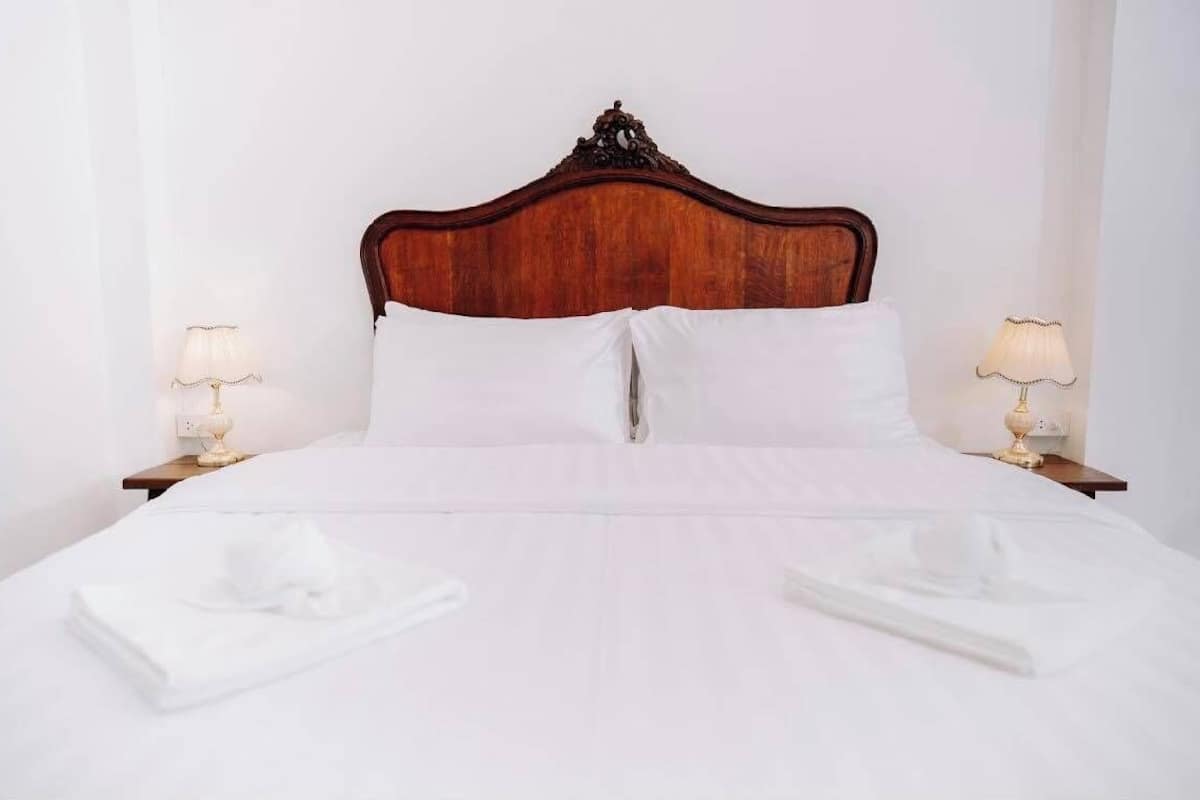 A neatly made bed with white linens, two bedside lamps, and a wooden headboard.