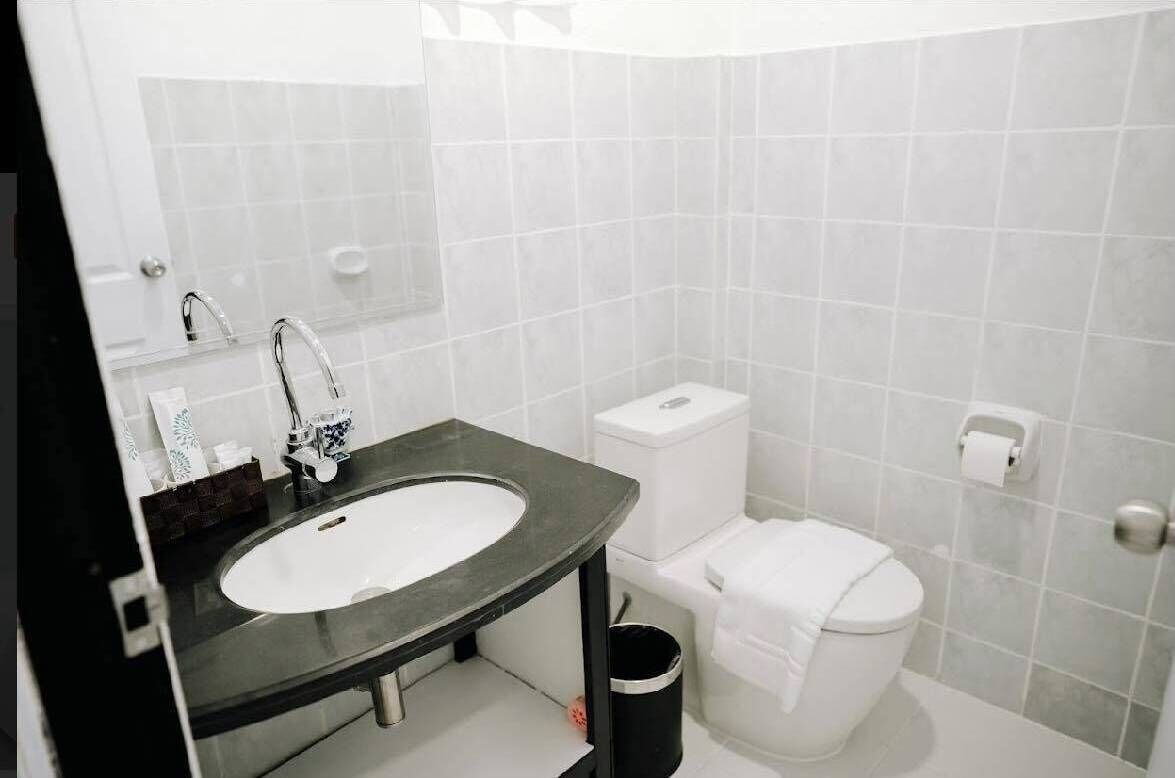 A bathroom with a white sink, a toilet, and a trash bin.