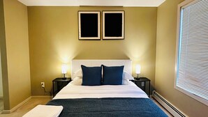 Habitación de hotel con una cama grande, dos mesitas de noche con lámparas, una lámpara de techo y una ventana con persianas.