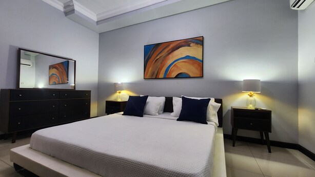 A modern bedroom with a large bed, two bedside tables with lamps, a dresser, and a large abstract painting on the wall.