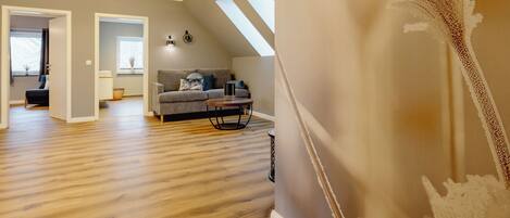 A spacious living room with a wooden floor, a grey sofa, and a ceiling light fixture.