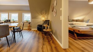 A modern living room with a dining area, a sofa, a chair, and a small table with a lamp. - Hünzinger Dorfschmiede - Holiday apartment Specht (Walsrode)