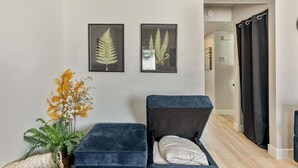 Un salon moderne avec un canapé, une petite table d’appoint ornée d’une plante, et deux reproductions botaniques encadrées accrochées au mur.