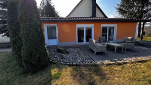 Une maison avec un toit en tuiles, un porche meublé de meubles en osier et un chemin de pierre menant à l’entrée.