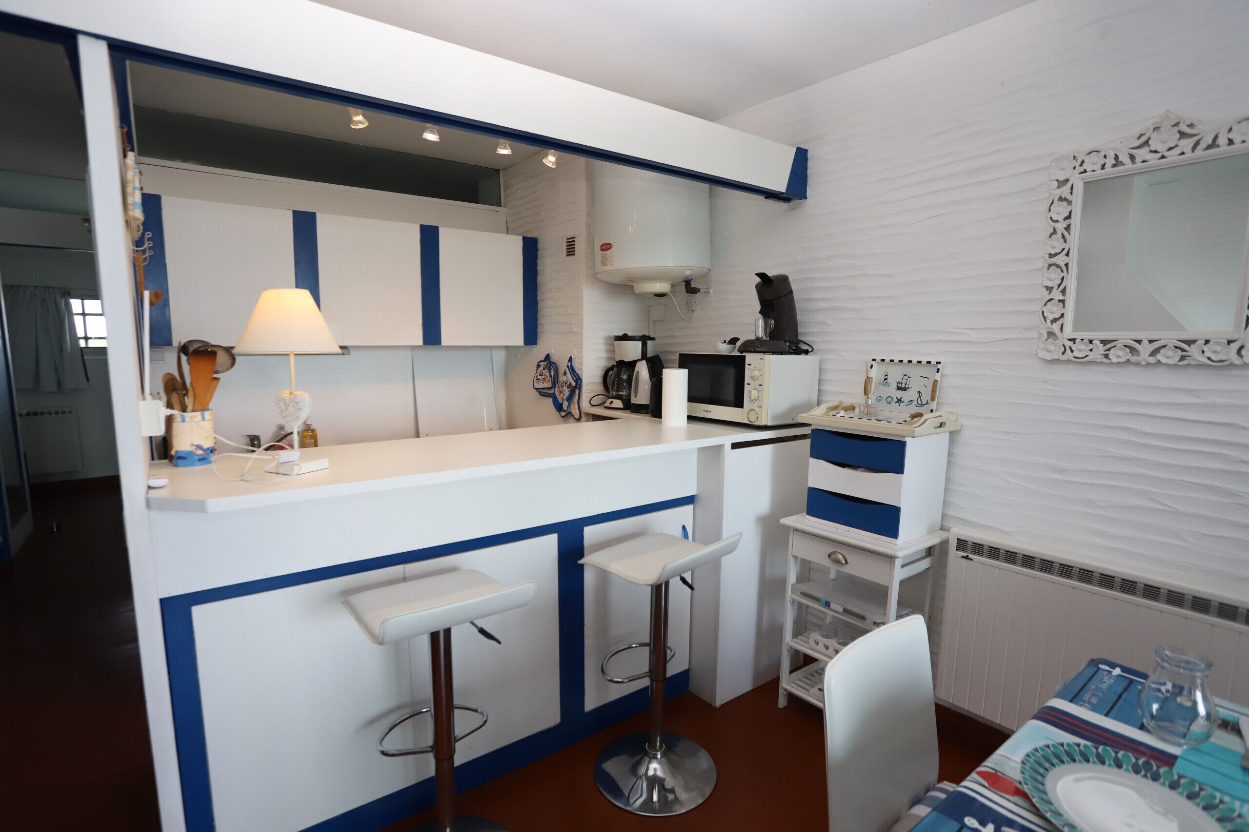 A compact kitchen with a white and blue color scheme, featuring a microwave, coffee maker, and a small refrigerator.