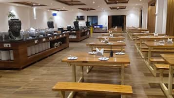 A restaurant with wooden tables and benches, a buffet counter with food items, and a television screen.