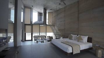Een moderne hotelkamer met een groot bed, een zithoek met twee stoelen, een kleine tafel en een trap naar een hoger gelegen verdieping.