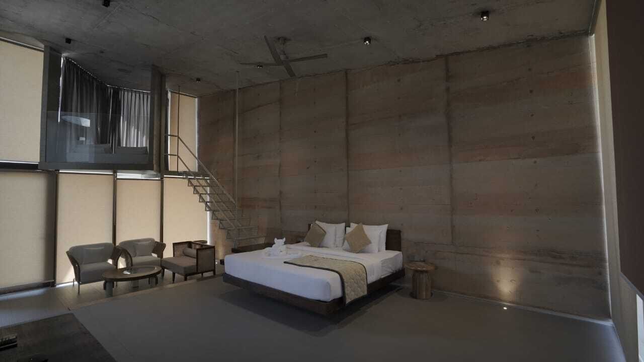 Een moderne slaapkamer met een groot bed, een bank en een kleine tafel. Er is een trap die naar een hoger gelegen verdieping leidt.
