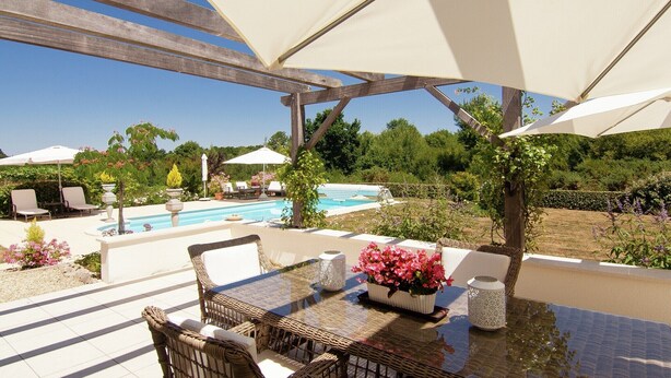 Un patio exterior con piscina, muebles de mimbre y sombrillas.