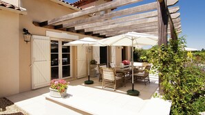 Un patio exterior con pérgola, mesa de comedor, sillas y sombrillas.
