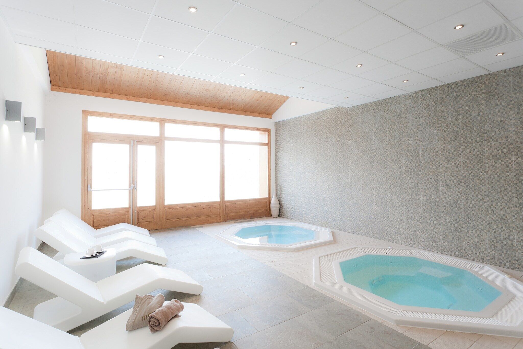 A modern spa room with two hot tubs and lounge chairs.