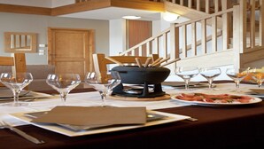 A dining area with a wooden table set for a meal, a black pot with utensils, and a staircase in the background.