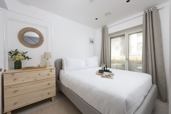 Een keurig opgemaakt slaapkamer met een bed, nachtkastje met lamp, spiegel en raam met gordijnen.