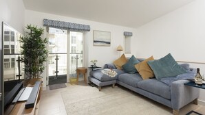 Ein modernes Wohnzimmer mit einem grauen Sofa, einem Holztisch, einer großen Topfpflanze und Blick ins Freie durch eine Schiebetür.