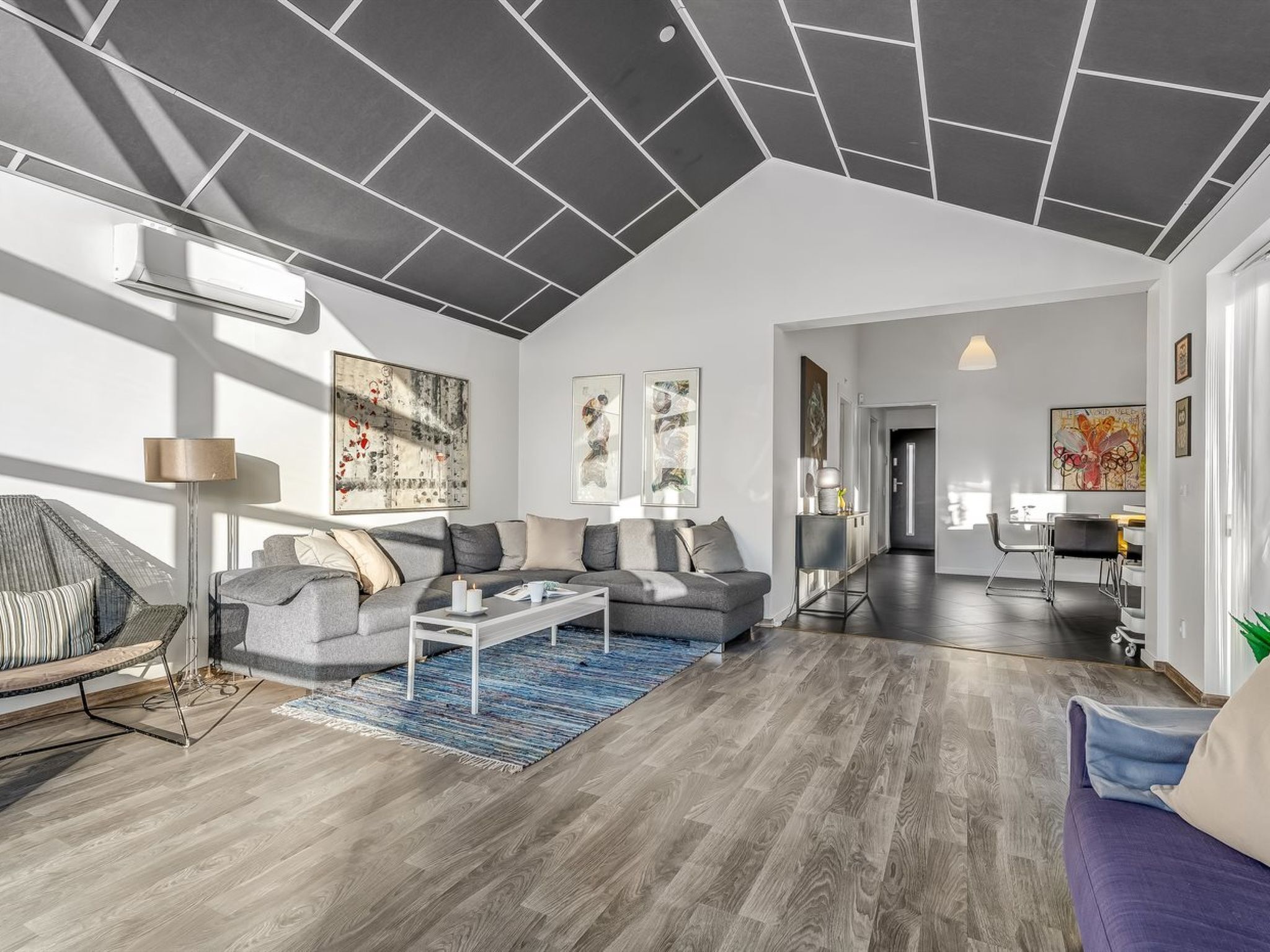 A modern living room with a sectional sofa, a coffee table, and a rug. There is a dining area with a table and chairs visible in the background.