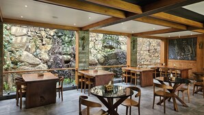 A restaurant with wooden furniture, stone walls, and a stone wall with a waterfall view. - The Story Resorts & Spa (Yercaud)