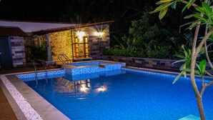 A swimming pool with a stone and tile border, a small adjacent structure with lights, and surrounding greenery. - The Story Resorts & Spa (Yercaud)