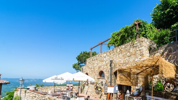 A stone building with outdoor seating and umbrellas, overlooking a scenic view.
