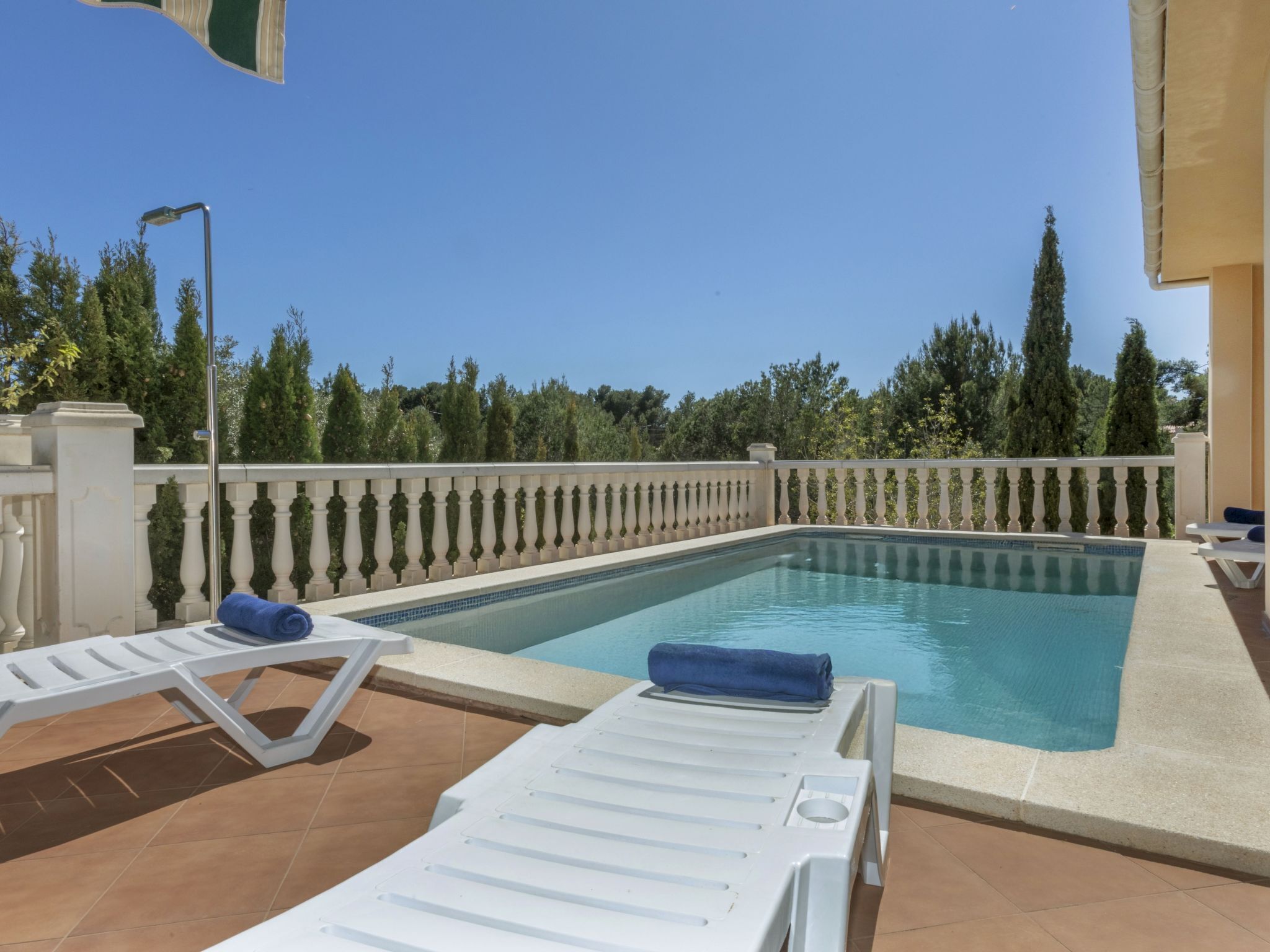 Un espace piscine agrémenté de chaises longues blanches et d’une serviette bleue, entouré d’une balustrade blanche et de verdure.