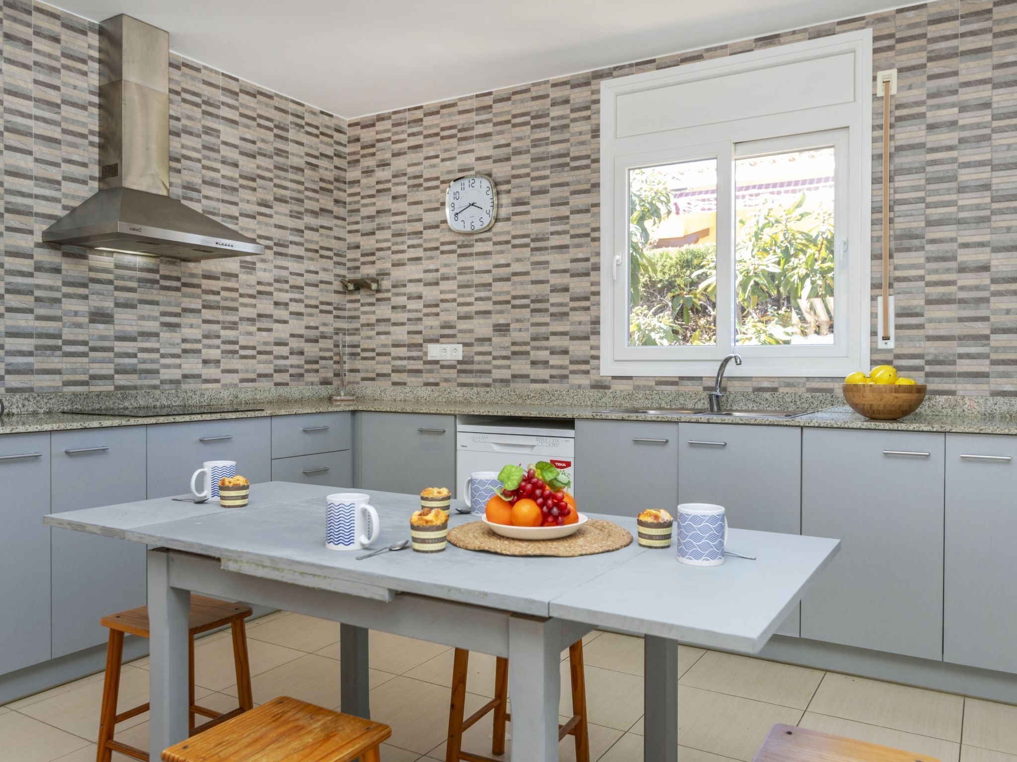 Una cocina moderna con armarios grises, una isla blanca y un ventanal con vistas al verdor.