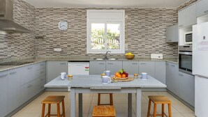 A modern kitchen with grey cabinets, a central island with stools, a clock, and a window with a view of greenery.