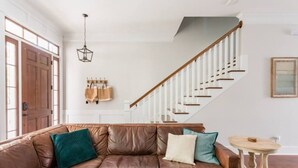 A living room with a brown leather sofa, a wooden staircase, and a small round table. - Liberty House - 3 Bedroom Downtown with Easy Parking (Savannah)