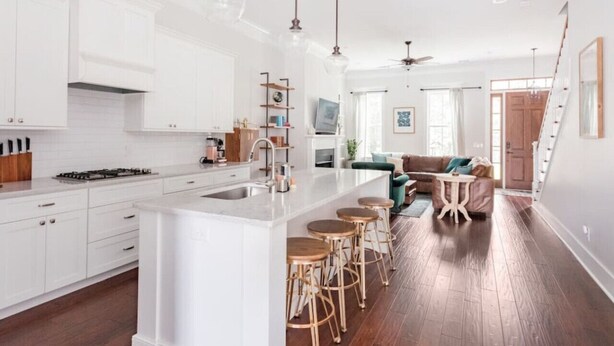 A modern kitchen with white cabinetry, a central island with stools, and a dining area with a green sofa and a small table. - Liberty House - 3 Bedroom Downtown with Easy Parking (Savannah)