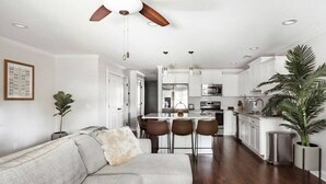 A modern kitchen with white cabinets, a dining area with a table and chairs, and a ceiling fan. - Garden Home at Liberty Estate (Savannah)