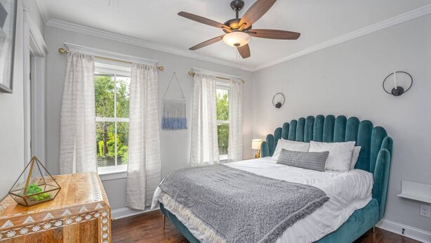 Een slaapkamer met een bed, een plafondventilator en een raam met gordijnen.