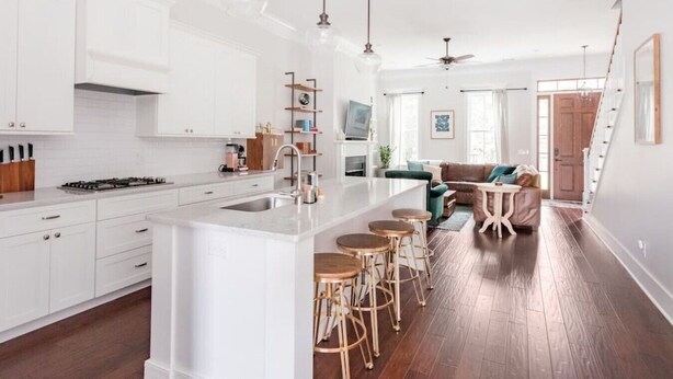 A modern kitchen with white cabinetry, a central island with stools, and a dining area with a sofa and chairs. - Radiant Estate in the Heart of Savannah (Savannah)