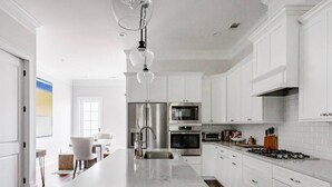 A modern kitchen with white cabinetry, stainless steel appliances, and a marble island. - Radiant Estate in the Heart of Savannah (Savannah)