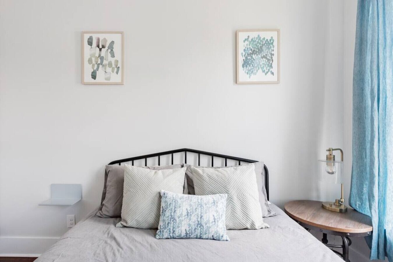 Une chambre à coucher avec un lit, des oreillers, une table de chevet, une lampe et deux œuvres d’art encadrées accrochées au mur.