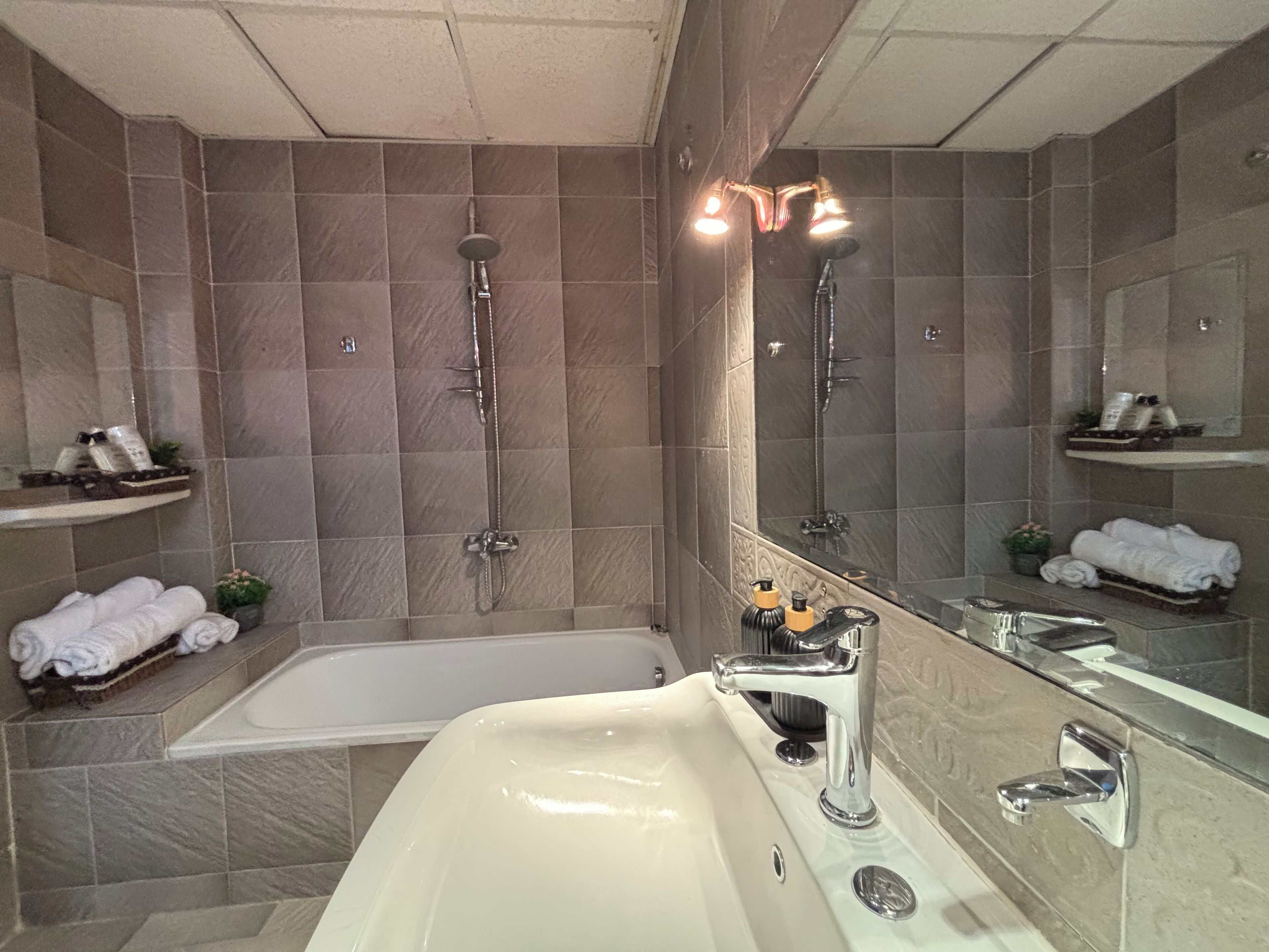 Bany modern amb banyera, un lavabo i plat de dutxa. Hi ha tovalloles i productes de tocador a les prestatgeries.
