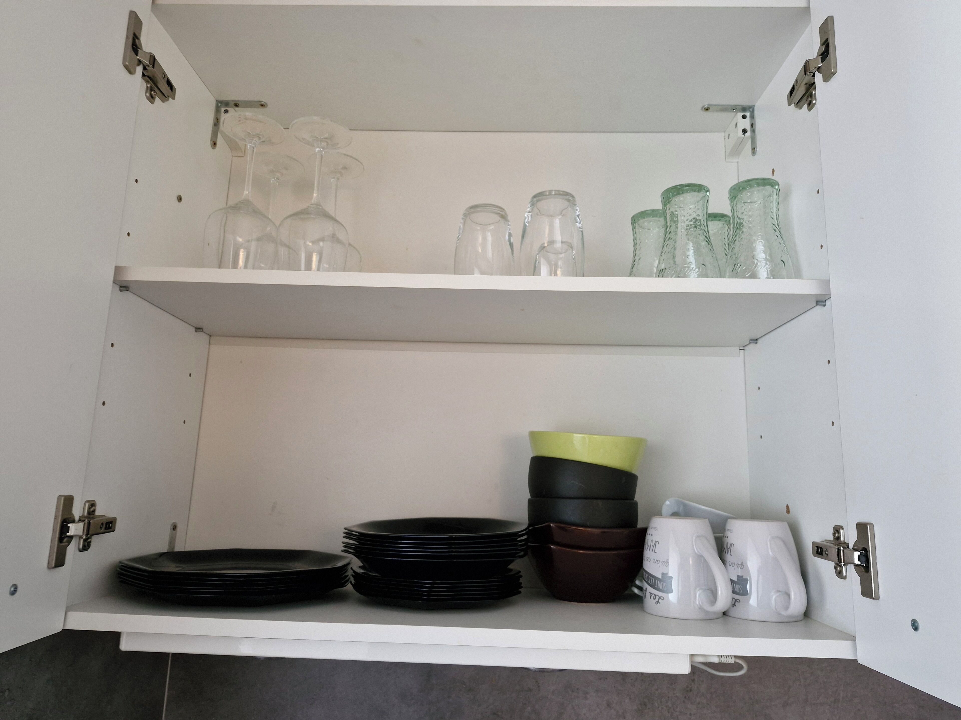 A kitchen cabinet with shelves holding plates, bowls, and glassware.