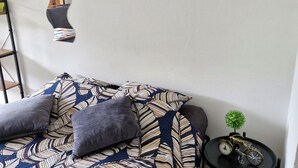 A modern bedroom with a patterned bedspread, a small round table with a clock and a bicycle, and a mirror on the wall. - Lovely studio 15min walk from Epinal town center (Chantraine)