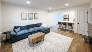 Un salon moderne avec un canapé d’angle, une table basse et un coin repas équipé de tabourets de bar.