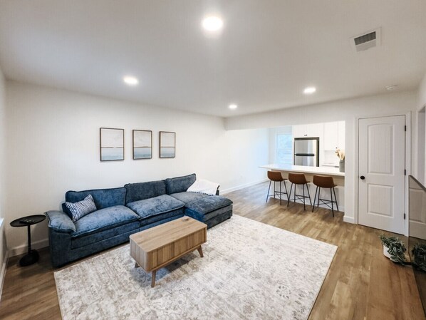 A modern living room with a sectional sofa, a coffee table, and a dining area with bar stools.