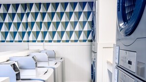 Une buanderie équipée de plusieurs machines à laver, avec un mur décoré de motifs et un sol carrelé.