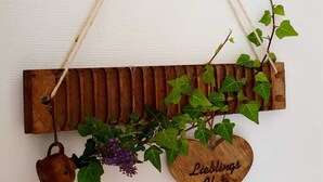 Un panneau mural en bois orné d’une plaque en forme de cœur sur laquelle est inscrit « Lieblings Platz », et une petite tasse en bois suspendue en dessous.