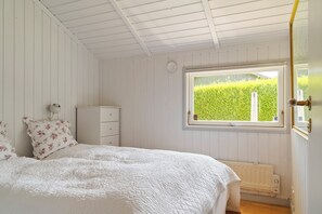 A bedroom with a bed, a dresser, a window with a view of greenery, and a radiator. - Super cozy holiday home in Marielyst (Væggerløse)