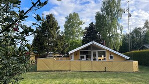 A single-story yellow building with a gabled roof, large windows, and a fenced yard. - Super cozy holiday home in Marielyst (Væggerløse)