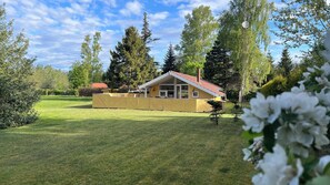 A yellow building with a red roof, surrounded by a well-maintained lawn and tall trees. - Super cozy holiday home in Marielyst (Væggerløse)