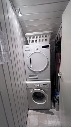 Un lavadero pequeño con lavadora y secadora apiladas, un tendedero y una puerta que da a un armario.