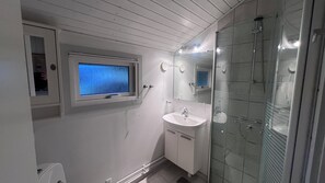 A bathroom with a window, sink, mirror, and glass shower enclosure.